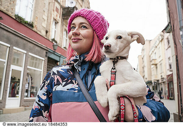 Smiling woman carrying cute puppy walking amidst buildings
