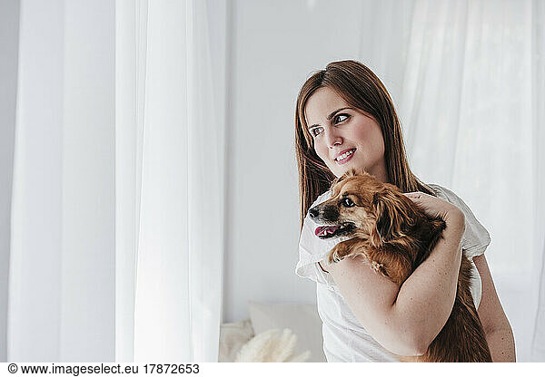 Smiling woman carrying dog at home