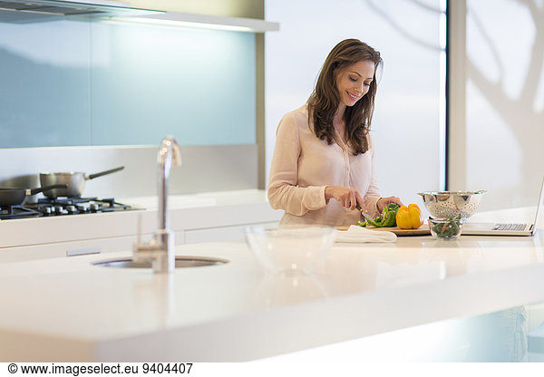 Smiling woman cutting bell peppers at modern kitchen counter