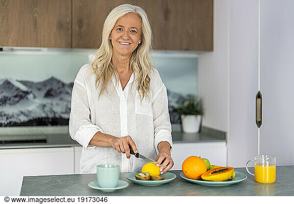 Smiling woman cutting fruits and making breakfast at home
