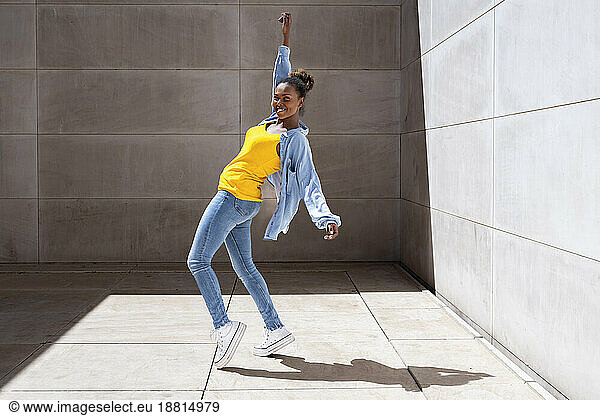 Smiling woman dancing near wall at sunny day