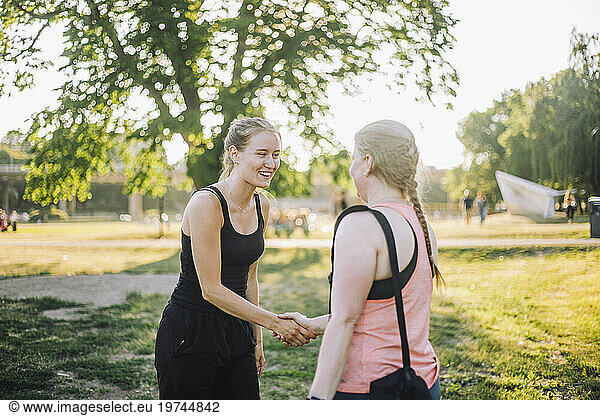 Smiling woman doing handshake with female friend at park