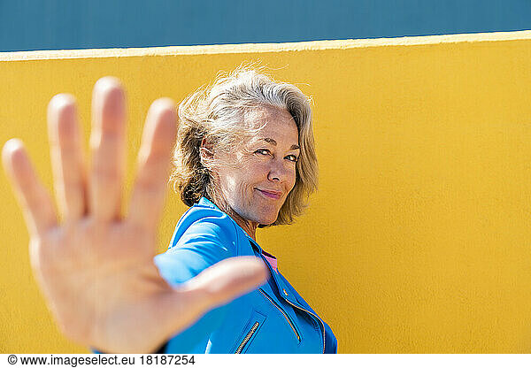 Smiling woman doing stop gesture by colored wall