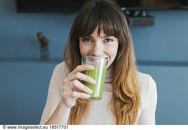 Smiling woman drinking detox juice at home
