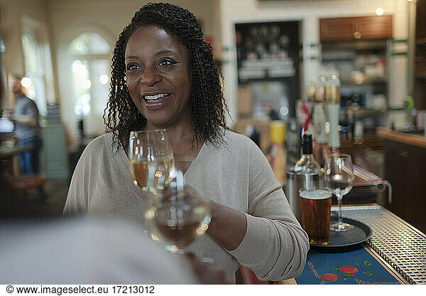 Smiling woman drinking white wine with friend at bar
