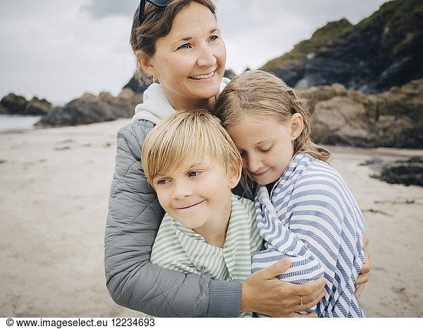 Smiling woman embracing kids standing at beach