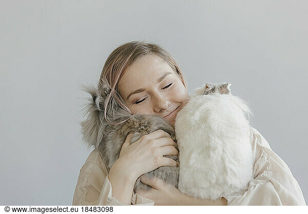 Smiling woman embracing rabbits in front of wall