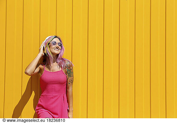 Smiling woman enjoying music listening through wireless headphones in front of yellow wall