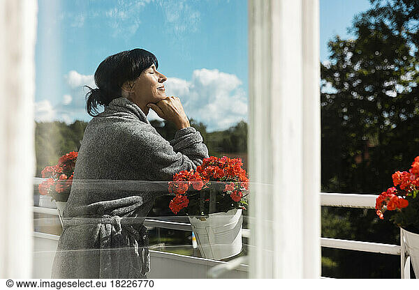 Smiling woman enjoying sunlight in balcony seen through glass