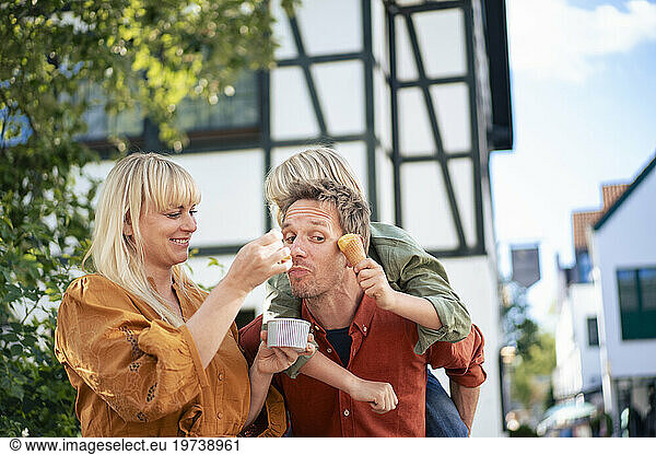 Smiling woman feeding ice cream to man giving piggyback ride to son