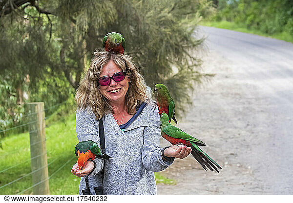 Smiling woman feeding king parrots on roadside