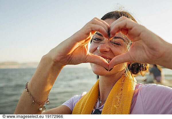 Smiling woman gesturing heart shape at the waterfront