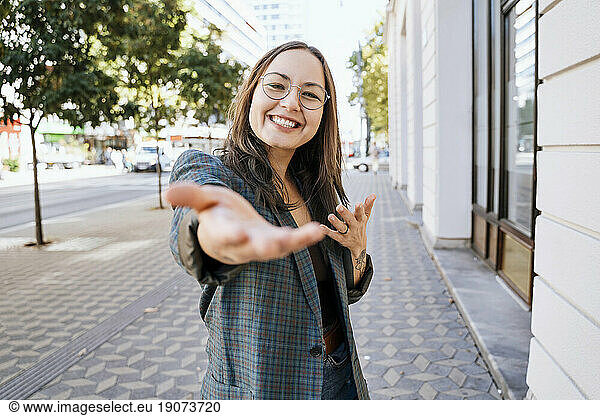 Smiling woman gesturing near building at footpath