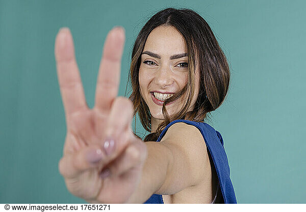 Smiling woman gesturing peace sign against blue background