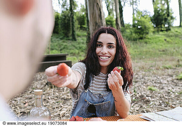 Smiling woman giving strawberry to boyfriend in forest