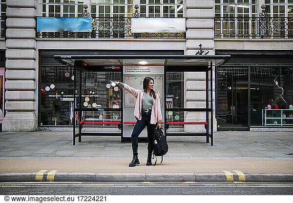 Smiling woman hailing while waiting at bus stop in city