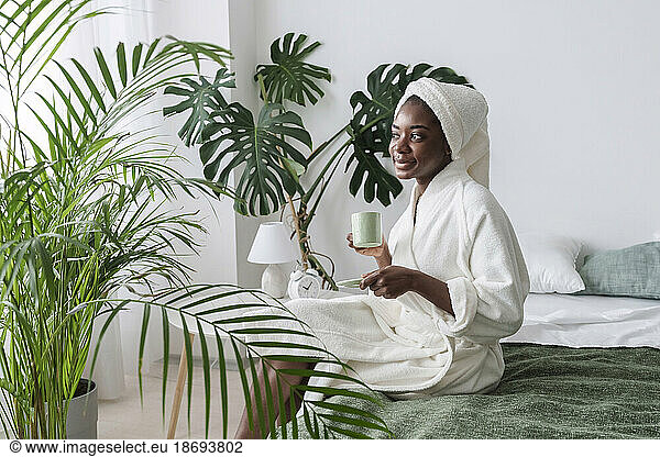 Smiling woman having coffee sitting on bed at home