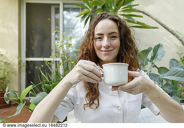 Smiling woman having cup of tea in backyard