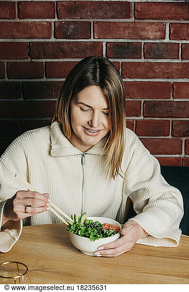Smiling woman having salad with chopsticks in cafe