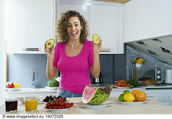 Smiling woman holding avocado in kitchen