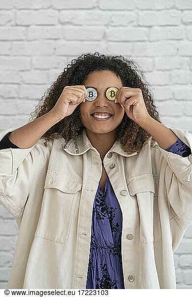 Smiling woman holding bitcoins in front of eyes