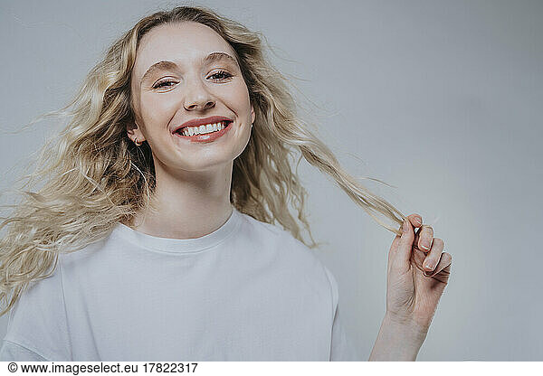 Smiling woman holding blond hair against grey background
