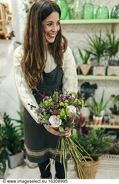 Smiling woman holding bunch of flowers while standing at flower shop