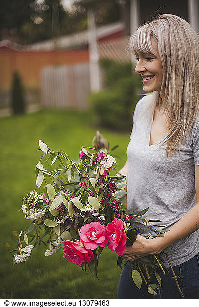 Smiling woman holding bunch of flowers while standing on field