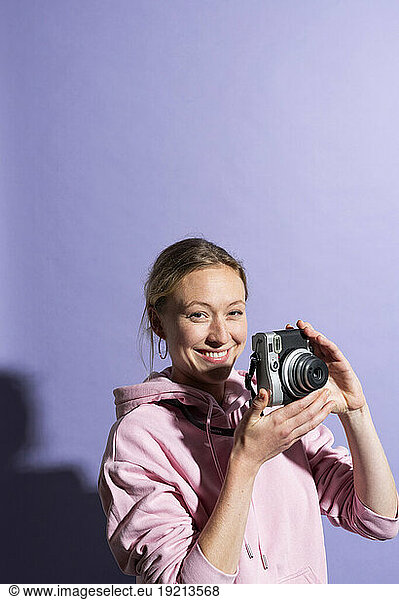 Smiling woman holding camera over purple background