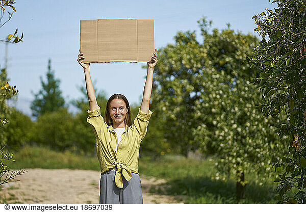 Smiling woman holding cardboard cut out with arms raised in garden