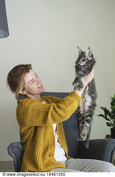 Smiling woman holding cat sitting in armchair at home