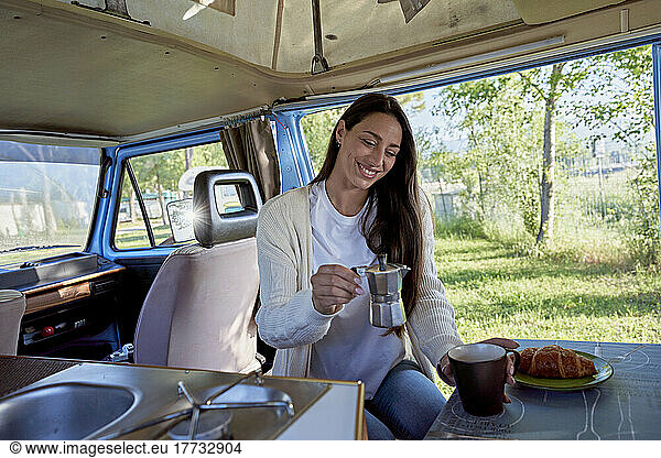 Smiling woman holding coffee pot by cup in motor home