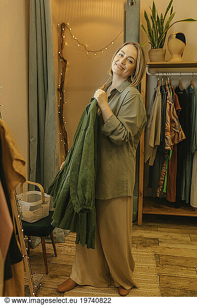 Smiling woman holding dress standing in store