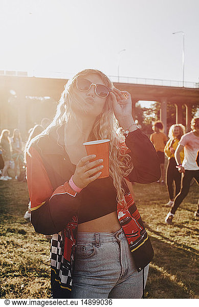 Smiling woman holding drink while standing at concert