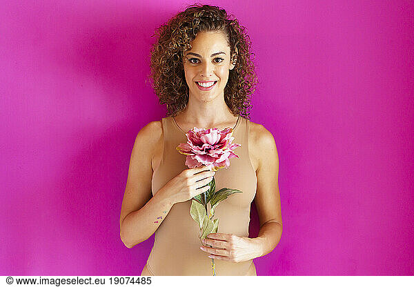 Smiling woman holding flower against magenta background