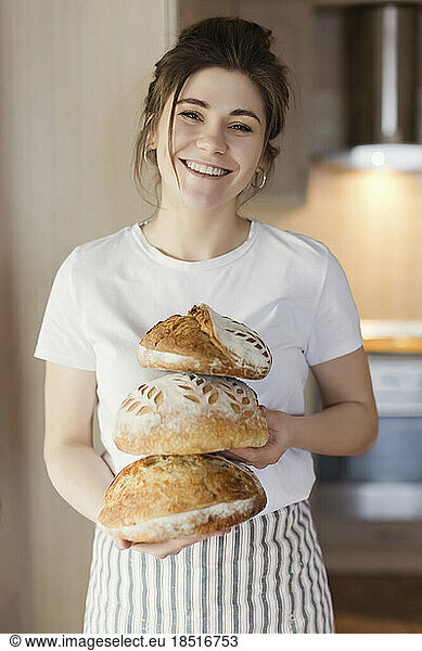 Smiling woman holding freshly baked breads at home