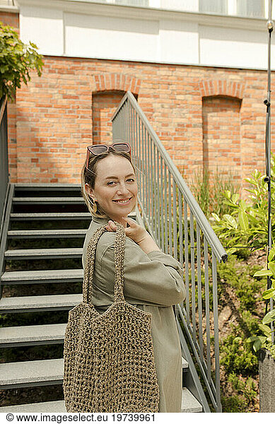 Smiling woman holding mesh bag near steps in front of building