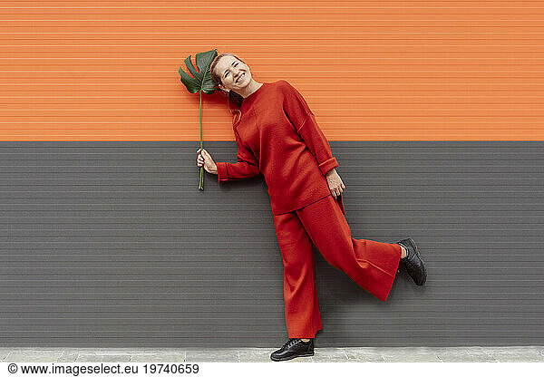 Smiling woman holding monstera leaf and standing near colored wall