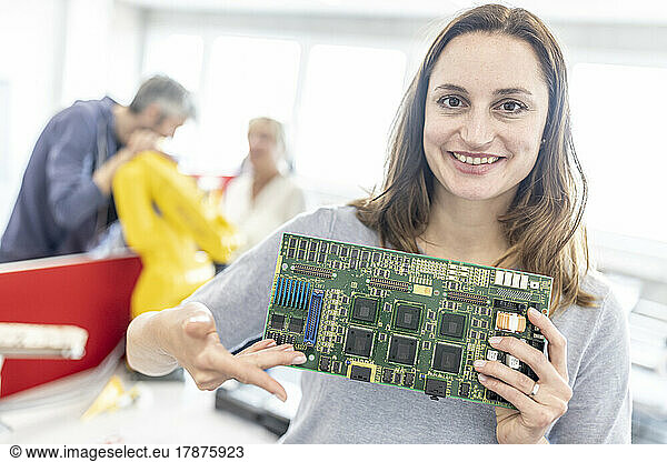 Smiling woman holding motherboard in factory