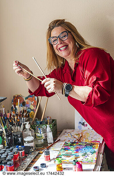 Smiling woman holding paintbrush while painting at home