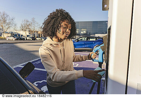 Smiling woman holding plug at electric vehicle charging station