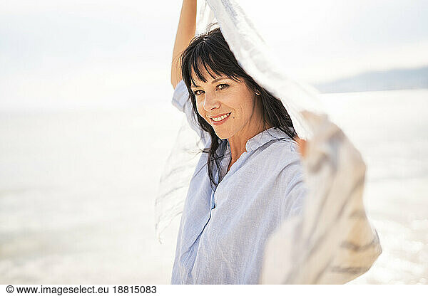Smiling woman holding scarf near sea at beach