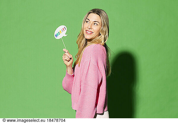 Smiling woman holding speech bubble with hurray text on it against green background