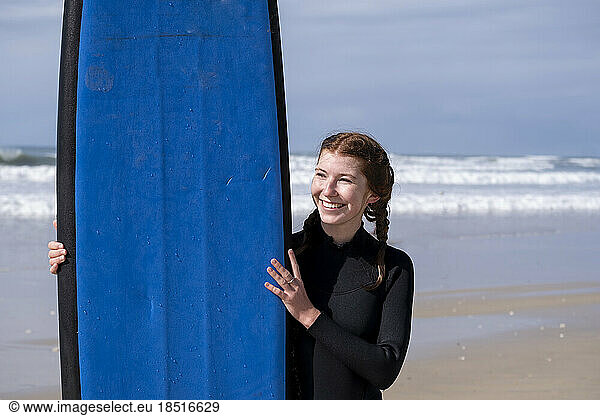Smiling woman holding surfboard standing at beach