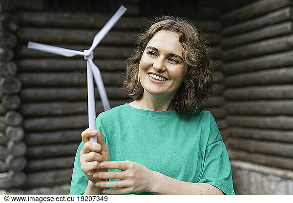 Smiling woman holding wind turbine model in front of log cabin