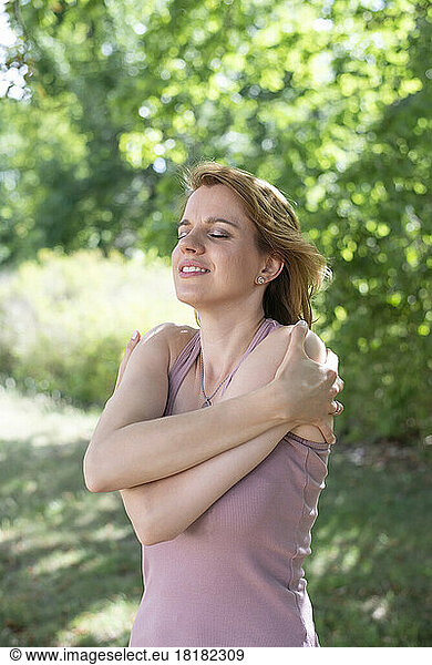 Smiling woman hugging self in park