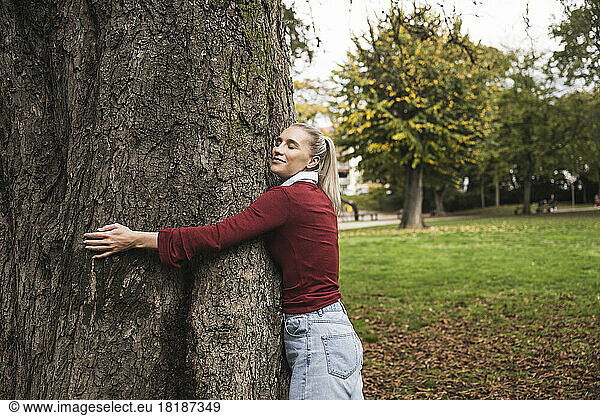 Smiling woman hugging tree at park