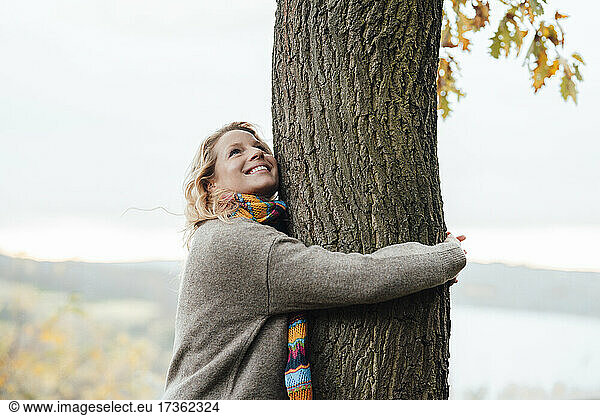Smiling woman hugging tree during autumn