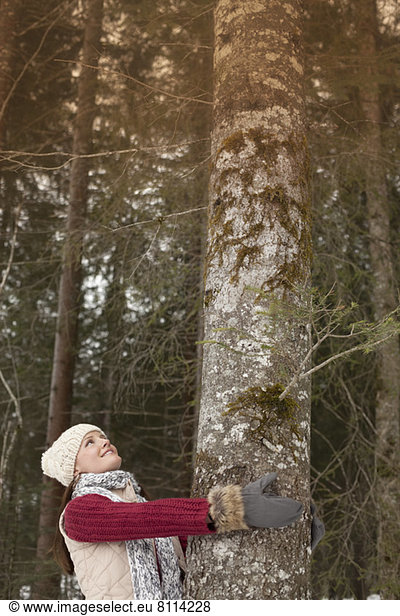 Smiling woman hugging tree trunk in woods