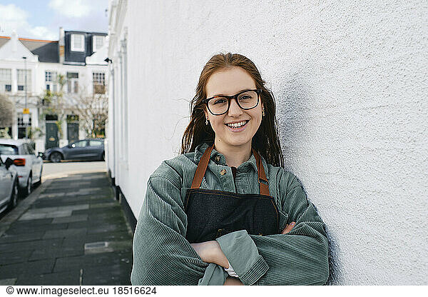 Smiling woman in apron with arms crossed leaning on wall